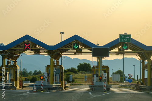 Obraz na płótnie Paid expressway checkpoint tollgate shows right direction on highway. Expressway green signs allow driving against hills at back sunset w salonie
