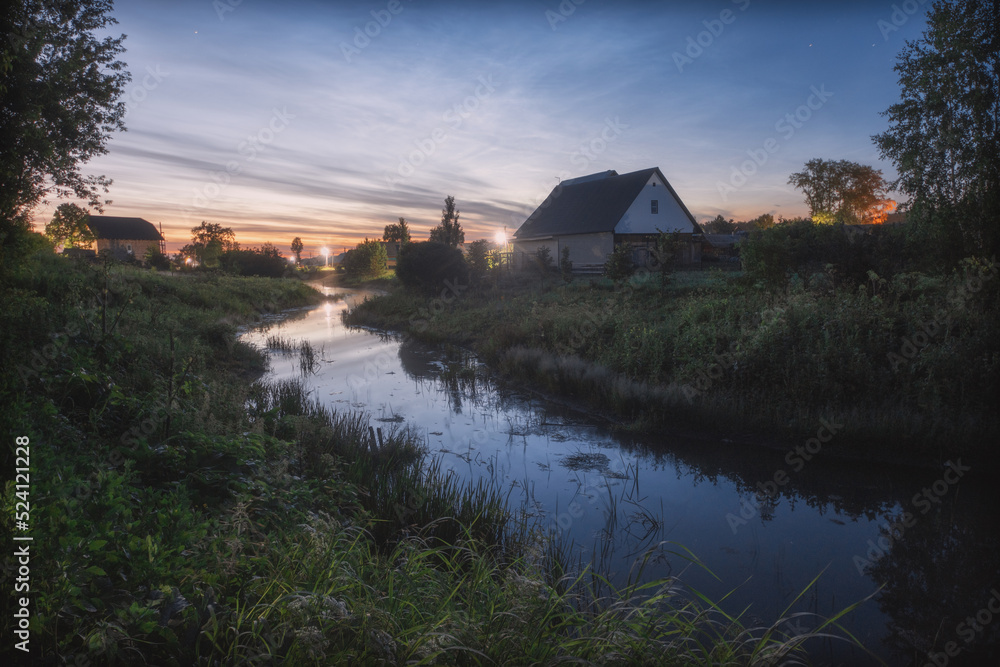 Landscape of dusk on the Kishertka river with houses in the countrside and noctilucent clouds, Russia, Permsky kray