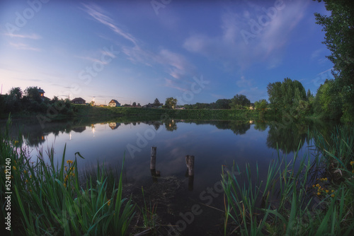 Landscape of white night on the Molebnoye lake with raft remnants, reeds , houses and clouds, Russia, Permsky kray