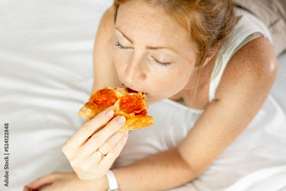 Cute woman redhead woman of 30s eating pizza and closes her eyes, feels pleasure from a good pizza. The concept of positive emotions and feelings. Cute woman redhead woman of 30s eating pizza and closes her eyes, feels pleasure from a good pizza. The concept of positive emotions and feelings.