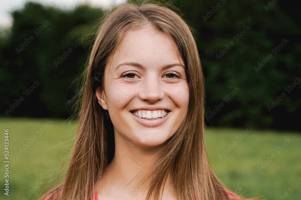 Portrait of happy girl smiling at camera outdoor with park on background - Focus on face