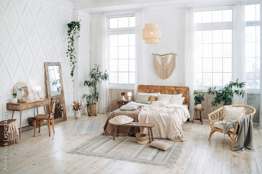 Cozy rustic bedroom with boho ethnic decor. Bright spacious apartment with large windows. Wooden furniture. Boudoir table. Large mirror. Handmade textile. Plants in the interior. Empty space