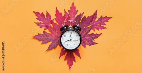 Hello, autumn. Dry wedge leaves in red color and alarm clock on orange background with copy space. Flat lay. Concept: autumn background, mock-up, postcard.