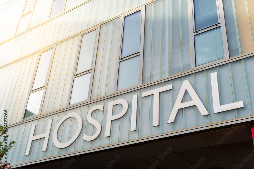 Hospital building sign closeup, with sky reflecting in the glass, healthcare and medicine concepts Hospital building sign closeup, with sky reflecting in the glass, healthcare and medicine concepts