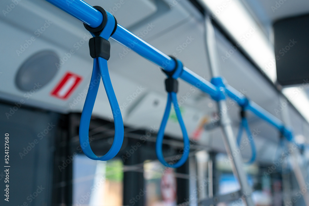 View from inside the city bus with passengers. Handles for standing passenger inside a bus. Bus hangers for people that are standing to hold on something during ride.