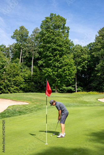 Male golfer putting, golf ball next to the hole with red flag, putt, golf game, green, bunker, trees