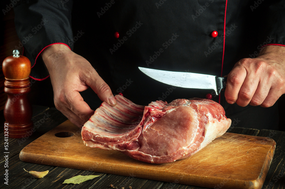 The cook or butcher cuts raw meat ribs on a cutting board before grilling. Meat dish idea for a hotel
