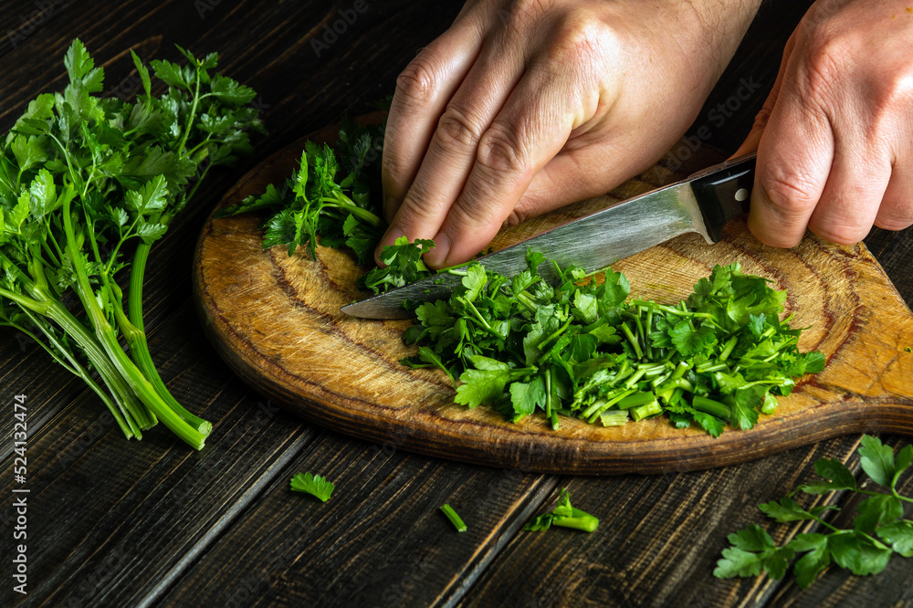 Professional chef cuts green parsley on a cutting board with a knife for preparing a vegetarian dish. Peasant food Professional chef cuts green parsley on a cutting board with a knife for preparing a vegetarian dish. Peasant food
