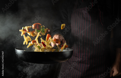 Cooking Thai food in a restaurant with fresh vegetables and pasta with spices. The chef throws food on a hot pan. Space for advertising on a black background.