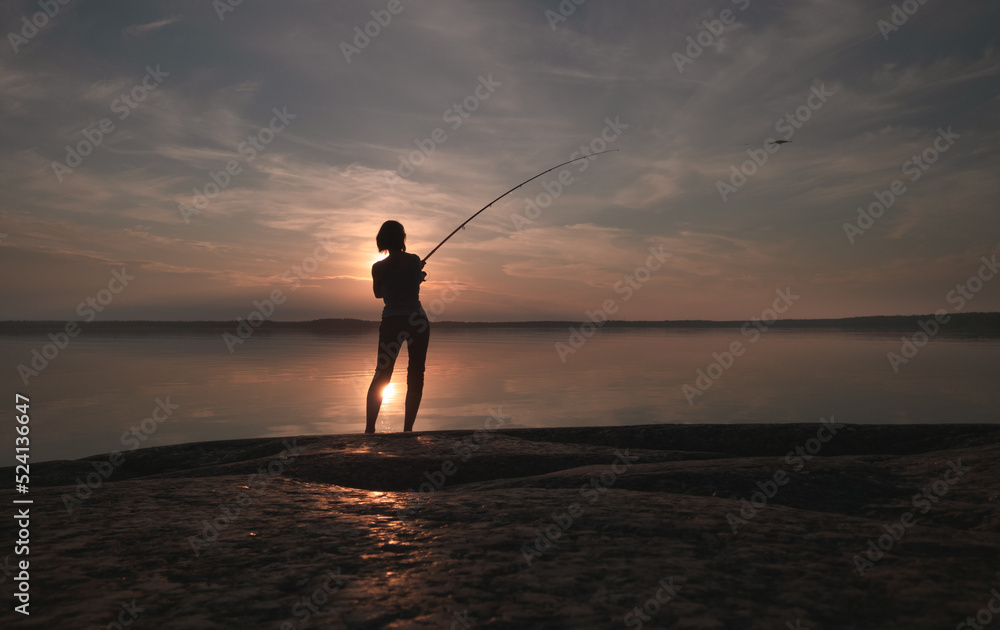 Girl in the process of fishing. Picturesque lake. Sunset sky.