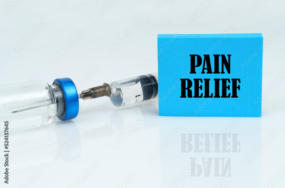 On a white reflective surface there is a syringe with an ampoule and a plate with the inscription - PAIN RELIEF On a white reflective surface there is a syringe with an ampoule and a plate with the inscription - PAIN RELIEF