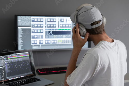 male producer in headphones doing music at home using computer