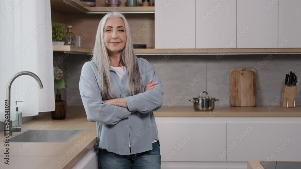 Happy senior lady caucasian mature 60s pretty grey-haired granny adult woman cheerful old female pensioner grandmother wears casual clothes looking at camera posing in kitchen studio with crossed arms Happy senior lady caucasian mature 60s pretty grey-haired granny adult woman cheerful old female pensioner grandmother wears casual clothes looking at camera posing in kitchen studio with crossed arms