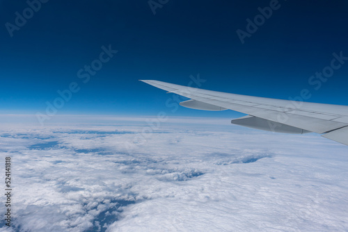 Wing of a flying plane over clouds on the blue sky.