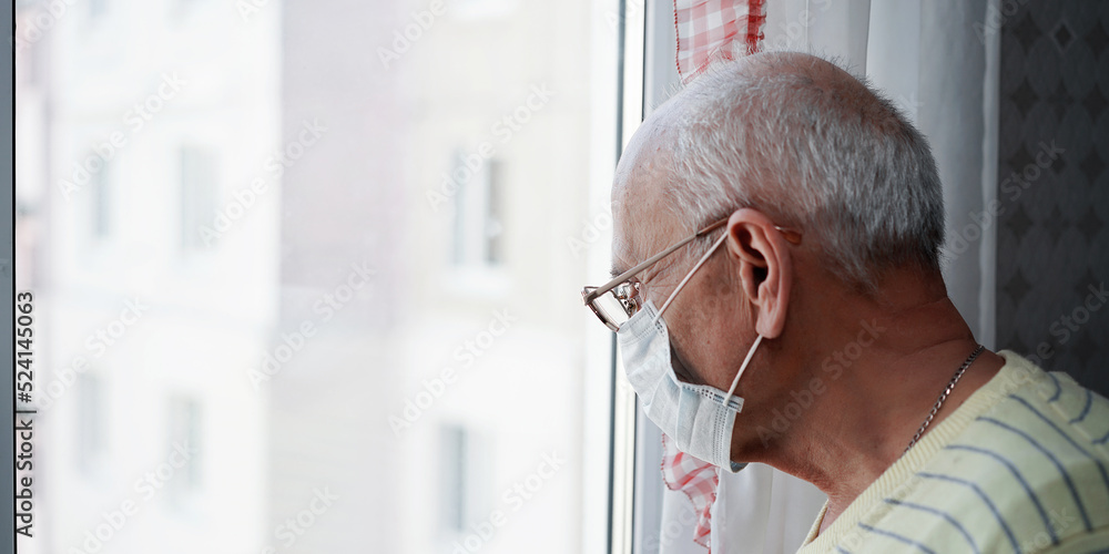 Lonely grandfather in glasses and face mask looking through window glass of nursing house Lonely grandfather in glasses and face mask looking through window glass of nursing house
