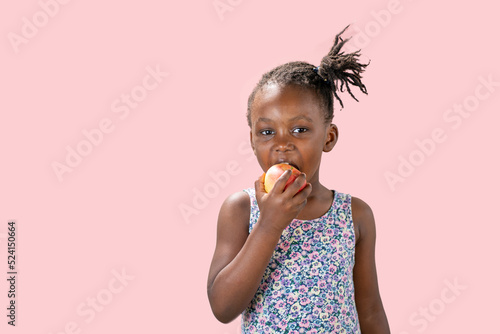 ritratto in studio isolato con sfondo rosa di bambina nera che mangia una mela  photo