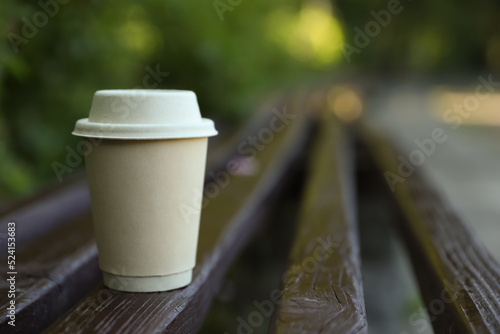 Cardboard takeaway coffee cup with lid on wooden bench outdoors, space for text