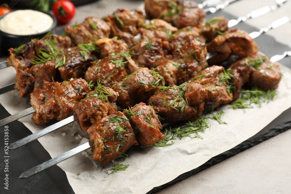 Metal skewers with delicious meat served on light grey table, closeup