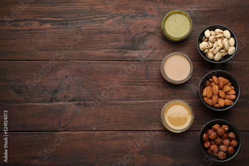 Different types of delicious nut butters and ingredients on wooden table, flat lay. Space for text