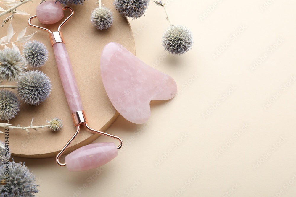 Flat lay composition with rose quartz gua sha tool and facial roller on beige background. Space for text - obrazy, fototapety, plakaty 