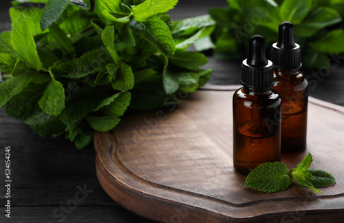 Bottles of mint essential oil and green leaves on black wooden table