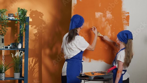 Young people painting apartment walls with orange color, using renovating tools to redecorate house interior. Using paint and paintbrush or diy equipment to renovate room at home. Tripod shot.