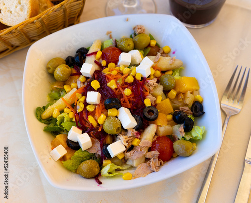 Appetizing salad of fresh greens with olives, pickled asparagus, canned tuna, grated beets and carrots, pieces of ripe mango and soft feta cheese served on white plate. Mediterranean dish..