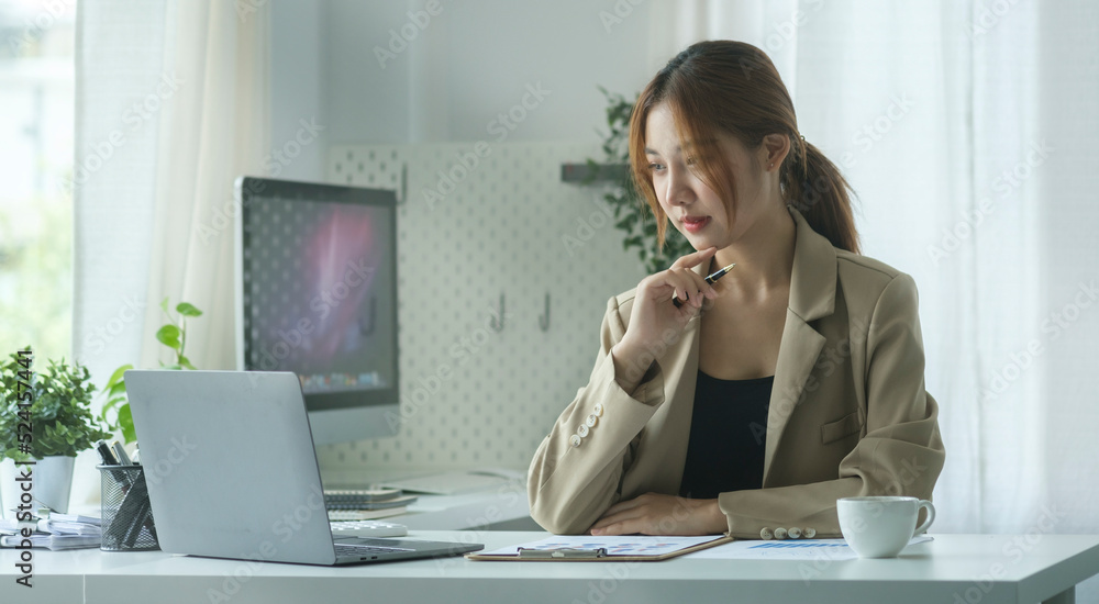 Focused young businesswoman reading online information on her laptop while sitting in modern office.