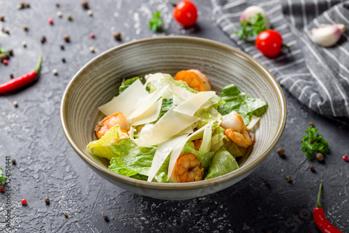 salad caesar with shrimps, mix salad and parmesan on plate on grey table
