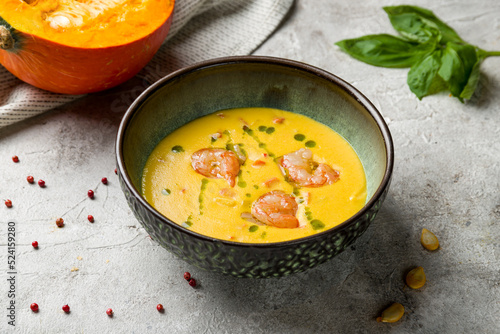 Pumpkin cream soup with shrimp and green oil on bowl on grey table