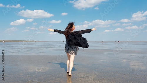 Rearview of beautiful young Chinese woman in black dress standing on muddy beach with white clouds and blue sky background in sunny summer day. Carefree girl enjoy her free time. Beauty lifestyle. #524160832