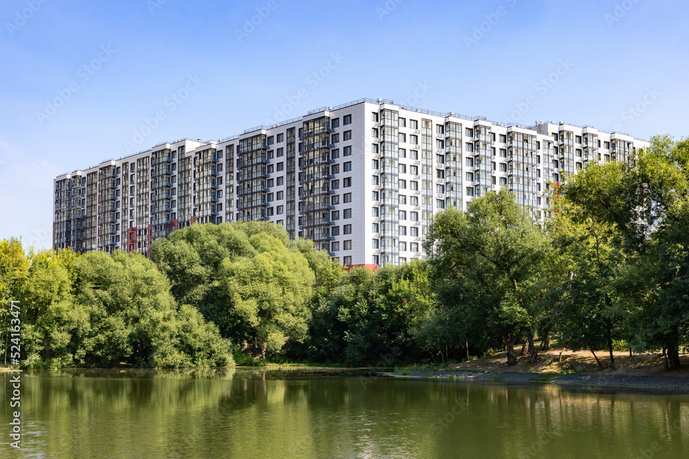 New modern residential apartment building near the lake surrounded by green trees	