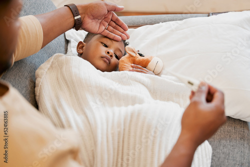 Sick, flu and cold child in bed, sad and ill with allergy and unwell at home with his worried mother. Parents hand on sons forehead for his temperature as she checks his fever with a thermometer