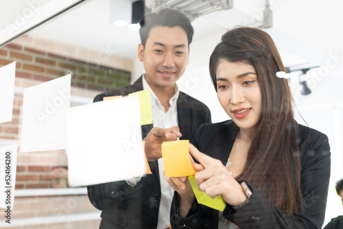 businesspeople office worker reading sticky notes on planning glass board. Business team pointing on keywords in sticky notes and business report to brainstorming about planning strategy of business. photo