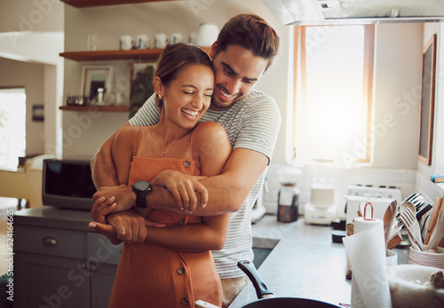 Love, romance and fun couple hugging, cooking in a kitchen and sharing an intimate moment. Romantic boyfriend and girlfriend embracing, enjoying their relationship and being carefree together photo