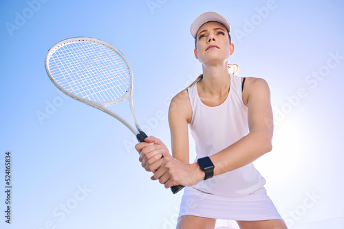 Professional tennis player, fit athlete and active woman playing sport, match and game with racket outdoors from below. Competitive, determined and serious female ready to serve, hit and play © Michael C/peopleimages.com