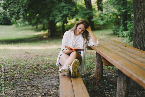 Woman holds book in her hands. Reading the book sitting on a bench at outdoors