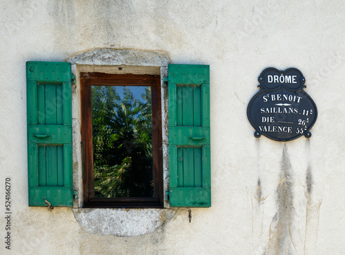 A window with green shutters and an old distance sign on a wall in St-Benoit-en-Diois in the Drome department, showing distances to Saillans, Die and Valence. photo