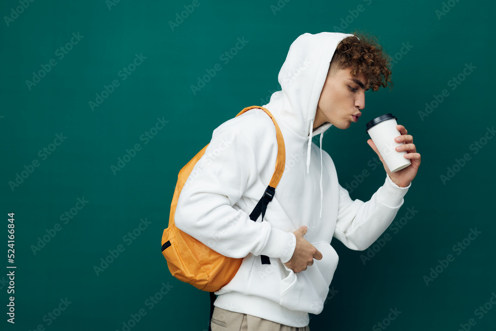 a nice man stands on a green background in a white hoodie with an orange backpack on his back and holding a glass in his hand drinks from it a nice man stands on a green background in a white hoodie with an orange backpack on his back and holding a glass in his hand drinks from it