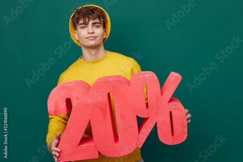 joyful, a man stands on a green background in bright clothes and holds a huge figure of twenty percent, red. Horizontal Studio Photography