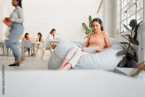 Serious, young design student relaxing and reading or listening to music in break room in startup office, with colleagues. Modern creative designer working on tablet in casual informal business photo