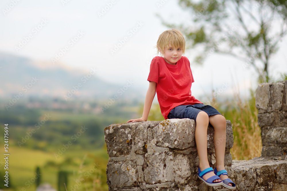 Naklejka premium Little child tourist visits famous fortress Rozafa near Shkodra city. Boy watching ancient stone walls and towers of bastion. Interest in history of children. Travel and tourism