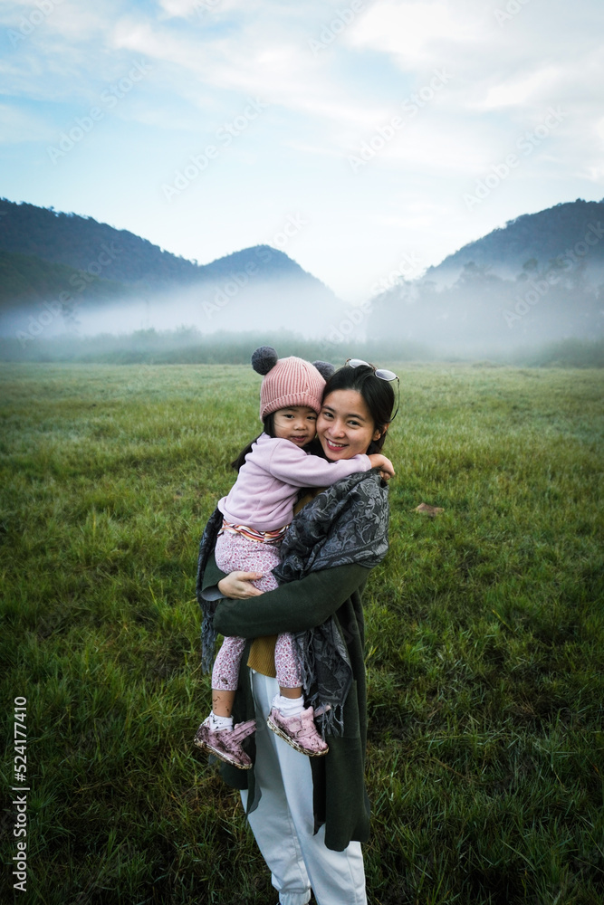 a mother is hugging her daughter on the grass field in the misty morning