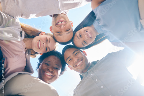 Diverse group of friends in a huddle together showing unity, trust and support outdoors in summer from below. International, happy and young men and women smiling, united and cheerful team outside photo