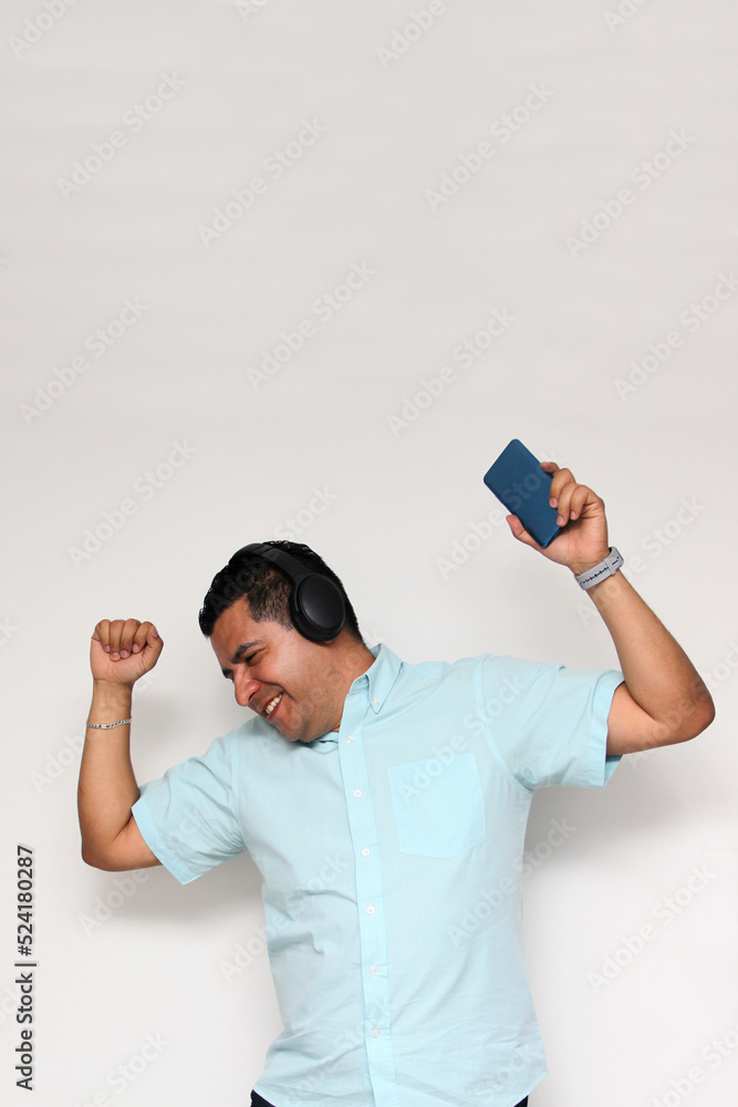 Latin adult man uses his wireless headphones and cell phone to listen to music, dance, relax and enjoy technology
