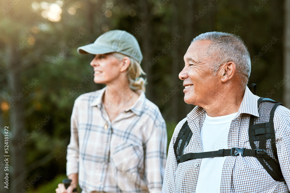 Mature man and woman hiking, smiling and looking at the view in nature. Fit local travel guide showing an active female tourist the natural landscapes while walking a trail outdoors in the wilderness