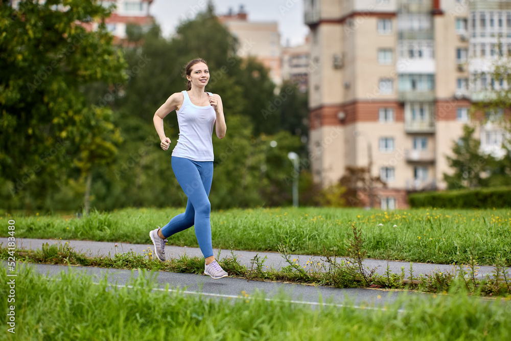 30 years old female runner jogging in a parked area of residential area with apartment buildings. 30 years old female runner jogging in a parked area of residential area with apartment buildings.