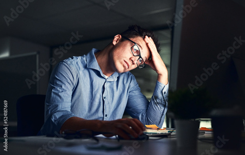 Tired, stressed businessman suffering from headache, working late night in the office. Serious, frustrated and overworked corporate male with headache staring at his screen in the dark.
