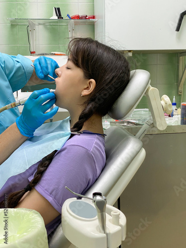 A girl sits in a dentist s chair  at a doctor s appointment  which she conducts an ultrasonic cleaning of her teeth.