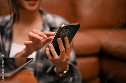 A beautiful asian female relaxing in her living room while using her smartphone. cropped shot.